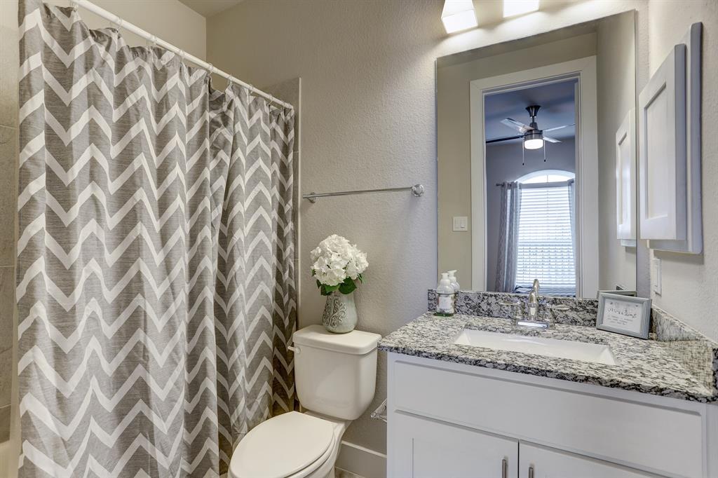 This en-suite bathroom boasts a lovely sink on a granite counter with storage space underneath, a large vanity mirror, and a shower with a tub.