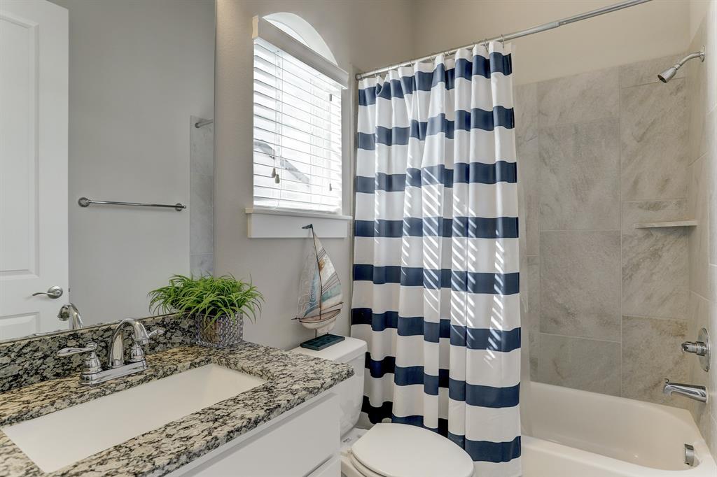 Another bathroom is decked with its own sink on a granite countertop, large vanity mirror, glass window, and a shower/bathtub with a stylish tiled-wall.