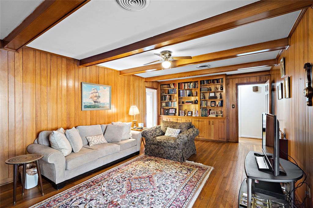 This welcoming, private den area features a wide library shelf soaring up to the ceiling. Edge to edge, original hardwood floors, walls, and wood beams surround its perimeter, bringing a warm, elegant feel to your hideaway.