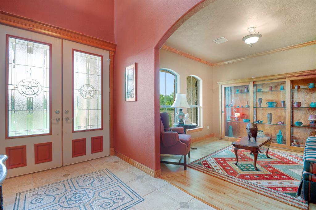 Main home double door entry reveals tiled foyer with mosaic tile inlay, high ceilings. A formal living with wood floors, large arched windows and crown moulding is just off of entryway and can easily be used for a study or home office area.