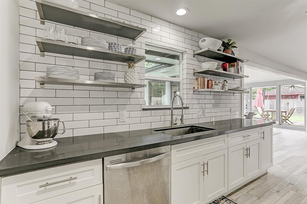 View of open-shelving, stainless steel dishwasher and updated sink. Full wall of subway tile makes this designer kitchen a standout.