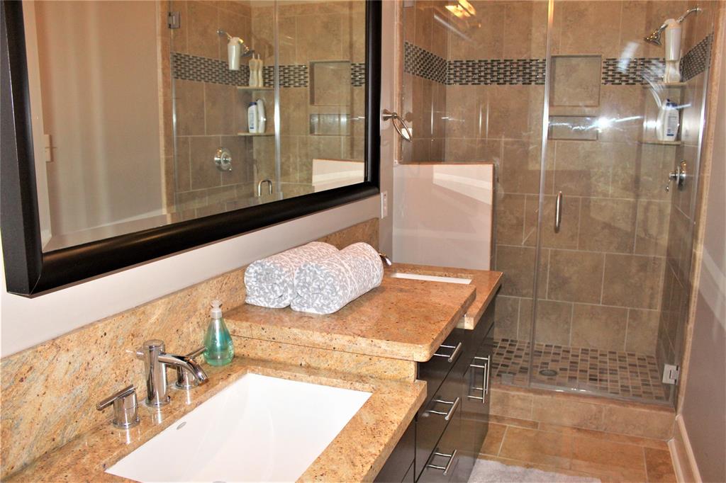 Second full bathroom with seamless glass door shower and double sinks.