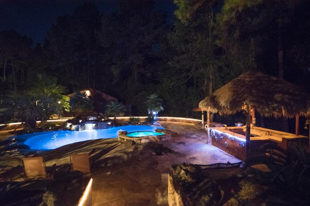 21919 Michael Drive Magnolia, Texas Retreat from big city hustle to this Colorado-inspired custom SHOWPLACE on 5 acres with resort-quality paradise pool/spa amongst towering trees of the Piney Woods! Beyond a private stone entrance gate, winding drive & Wisteria-covered bridge, this picturesque home features a refined log cabin design, wrapped in Austin limestone accents. This open concept floorplan features warm, cedar walls, soaring ceilings, backlit marble accents, stainless apps, granite counters and marble and onyx floors. Primary BR suite features luxe custom upholstered window coverings, LED-accented crown moulding, marble flooring and a huge walk-in closet that is second to none. Grounds are heavily wooded with rolling topography. An English-style butterfly garden, pergolas & fountains boasts dramatic nighttime illumination that are equal parts serene and surreal. The home also has a 2,400 SF metal building & custom Harley garage for classic car enthusiasts. Great schools & easy access! Never flooded!