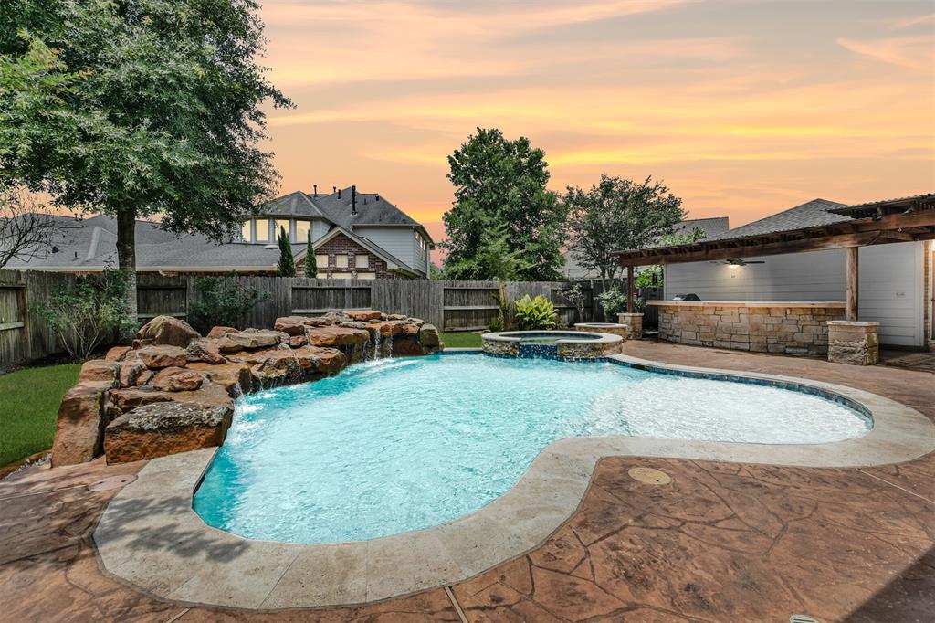 7603 Garden Knoll Lane Humble, Texas Beautiful home with stunning curb appeal & fabulous back yard complete with pool/spa, cascading waterfall, outdoor kitchen, mosquito mist system & covered patio. 2021 roof and 2018 pool/spa. The front of this home is so charming with a wraparound brick porch & classic brick & stone exterior. Inside you will love the private study & elegant dining room. The soaring ceilings in the family room will wow you along with the gorgeous kitchen with 5-burner cooktop & plenty of counter space. Features include a curved staircase with wrought-iron spindles, crown molding, curved arches, blinds, water softener, a double-sided gas-log fireplace & built-ins. The quality is obvious from the moment you step in the door. The primary retreat welcomes you with a fireplace & spacious sleeping area. The spa bath has both a jetted tub & shower, a long vanity with 2 sinks & an amazing closet. Upstairs you will find 3 bedrooms & 2 baths, a large game room & an extra room for a study area, media room or gym.