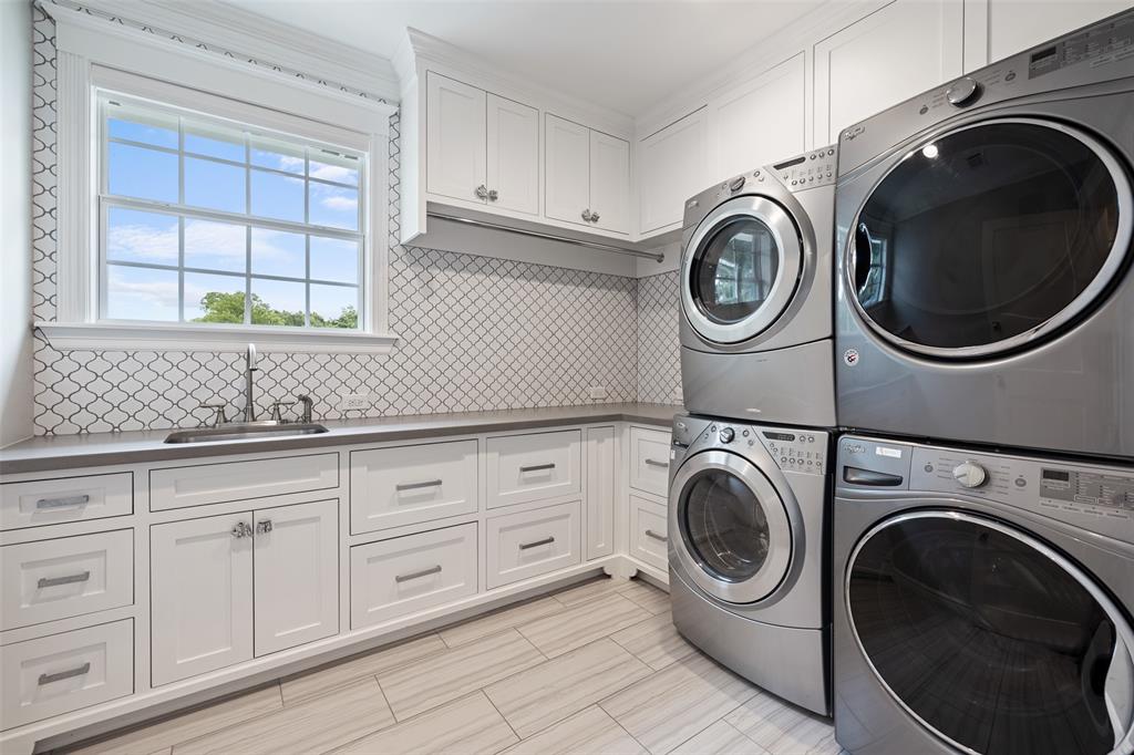 This large utility room is serious business. It's equipped to accommodate double stackable washer and dryers. It also includes a built-in sink, custom built-ins with a draw for clothes for each bedroom, hanging rod, quartz countertops, and white ceramic backsplash.
