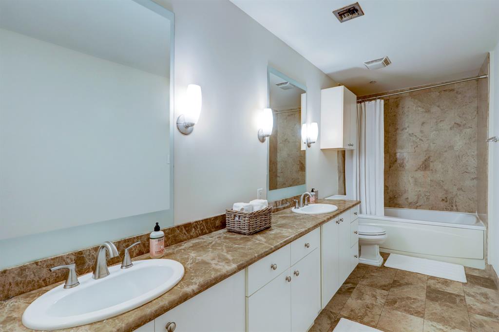 Larger bathroom en suite including dual sinks and granite countertops with neutral tile.