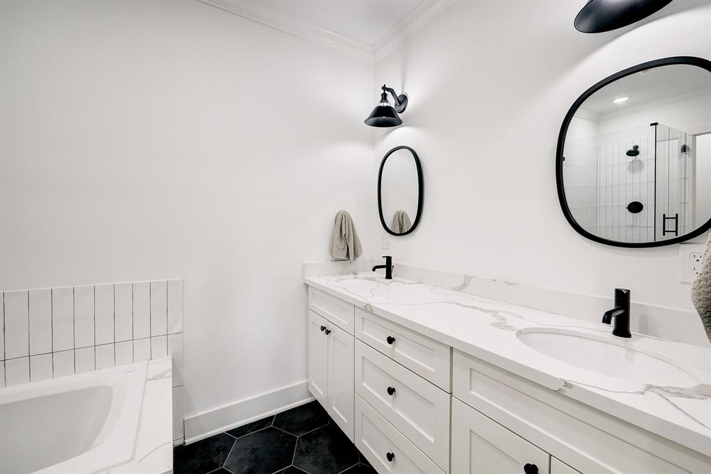 The elegant primary bath is crisply outlined in white and black with recessed ceiling and mounted light fixtures, and includes a dual bowl vanity.
