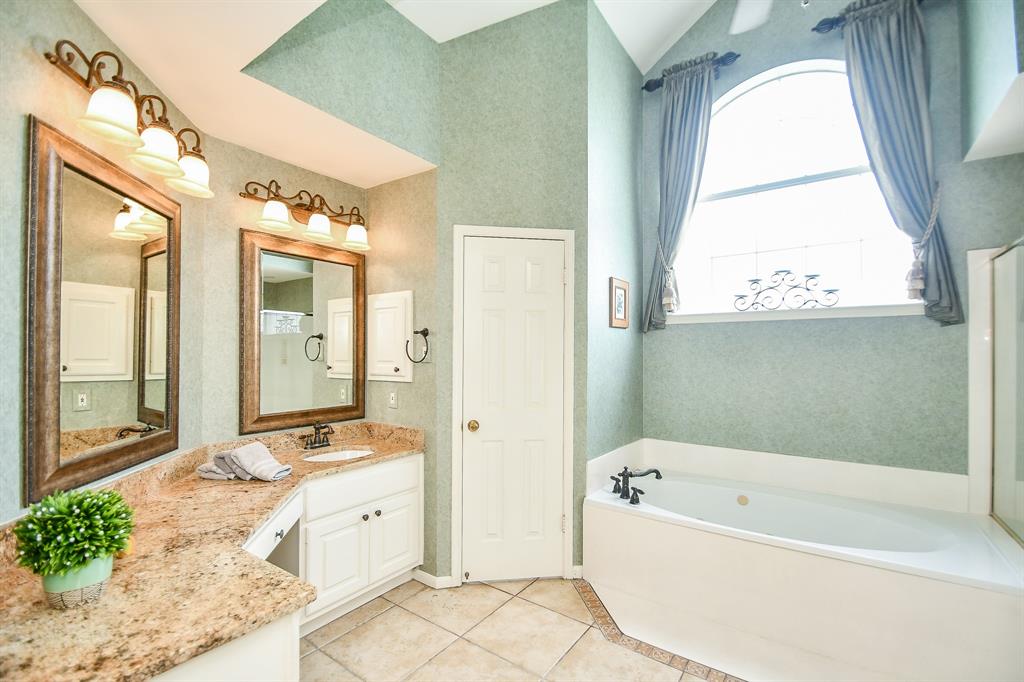 Serene natural tones surround the soaking Hollywood tub under a delightful arched window. Caramel toned granite countertops host separate sinks/vanities, with gorgeous framed wall mirrors, above.