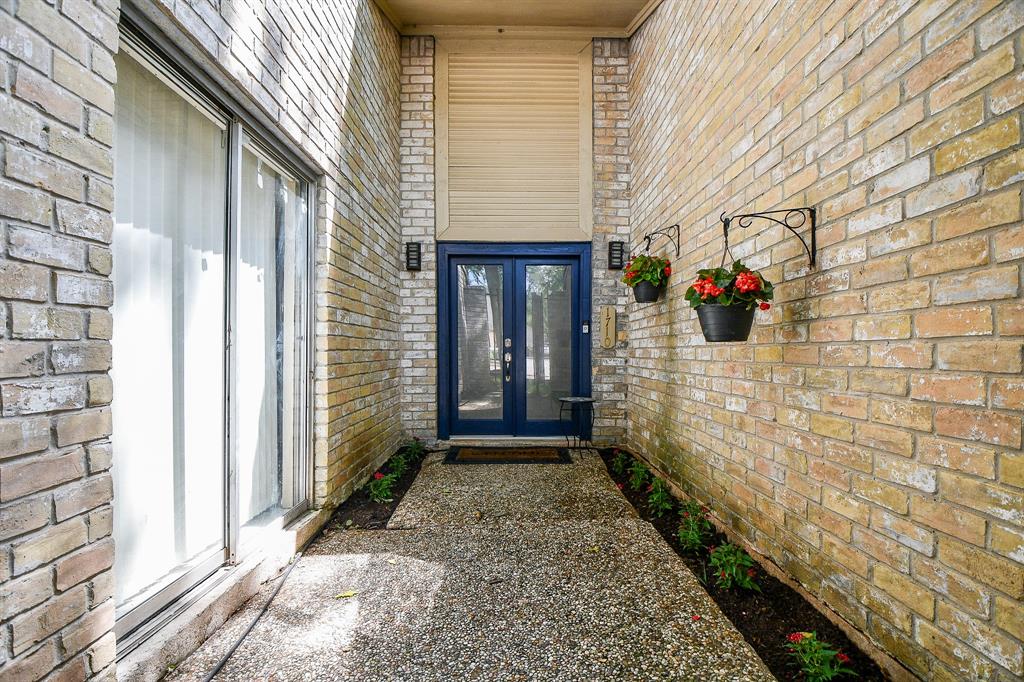 The main covered entrance welcomes with a splash of color on double doors, sharing this divine courtyard-like area with double patio doors, left, and charming planting beds.