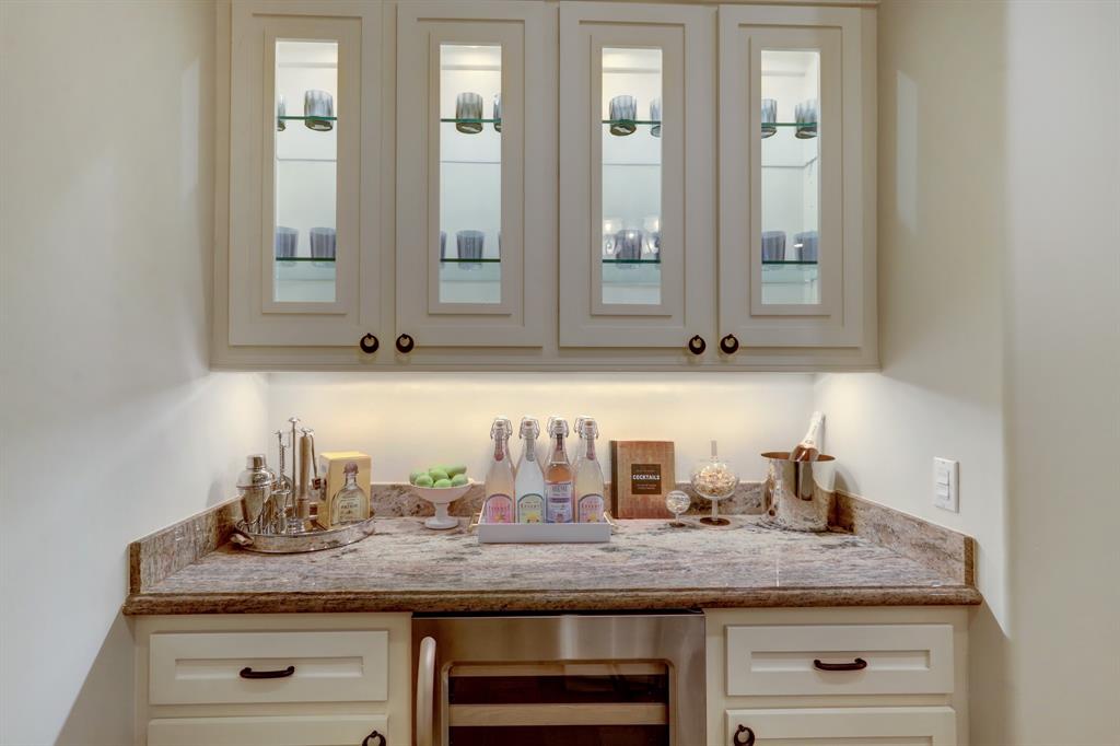Dry-Bar with Slab Granite Counter, Built-In Glass Fronted Cabinetry with Glass Shelving and Lighting, Wine Chiller and Under-Counter Storage Cabinets.