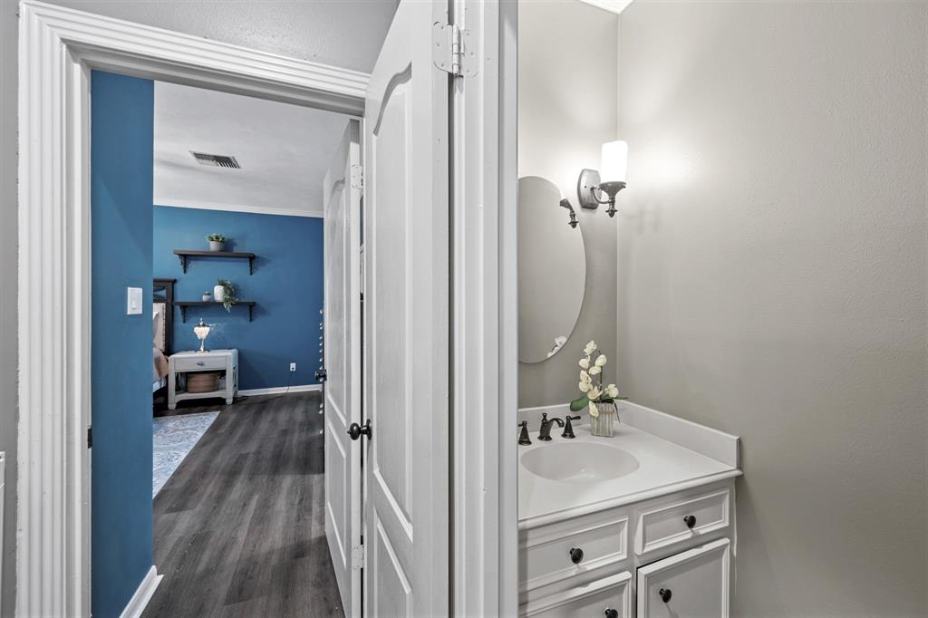 A half bathroom is conveniently located near the first-floor main living spaces for your guests, complete with a lovely white sink vanity, chic frame-less mirror, and custom sconce lighting.