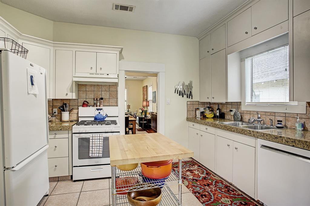 The crisp, white kitchen has granite counter tops, a gas range, dishwasher, small free standing island and a window over the sink.