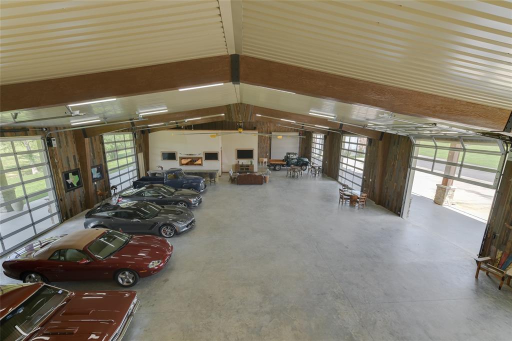 The INTERIOR (100 X 58)  includes an over-sized industrial fan, exposed wood beams, metal roofing, concrete flooring, fluorescent lighting, Wet Bar with seating for 6/stone counters and mirrored backsplash/2 stainless sinks/2 Monogram stainless mini-refrigerators/Hushizaki stainless ice maker, 3 TVs, three entrances to the attached housing/dining/kitchen facility, doors to several storage lockers.