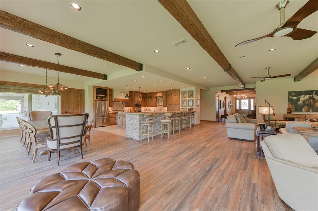 View of the open floor plan from the LIVING ROOM facing toward the DINING AREA (19 X 14) and nearby KITCHEN (19 X 19). The Dining Room includes the same hardwood flooring, exposed beams and windowed area as the Living Room.  The Kitchen features tile flooring, center island, wet bar with hammered copper sink, breakfast bar seating, stone counters, stained wood cabinets/drawers, 2 stainless sinks, stainless Zephyr/GE/Dacor/Scottsman appliances - everything needed for the visiting chef!