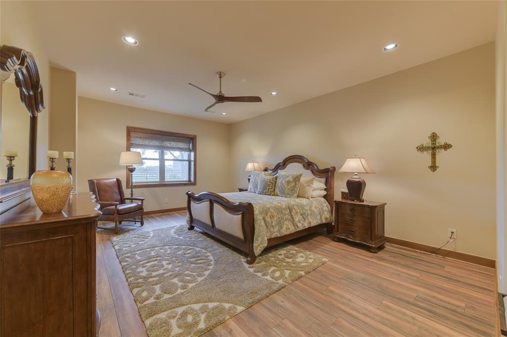 One of two GUEST BEDROOMS on the Barndominium\'s first floor - this one (34 X 15) features hardwood flooring, 2 dual fold closets with shelving, window with shades, recessed lighting, ceiling fan and en suite bath (granite counter/tile flooring/wood framed mirror/dual sinks with cabinets below/walk-in frame-less glass shower with tile surround/light sconces.