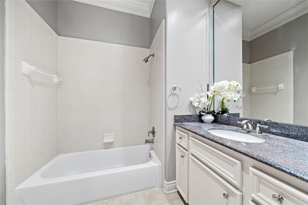 The secondary ensuite bath features an alcove tub and a full vanity area with granite countertops, a large mirror, and plenty of storage space for bathroom essentials.