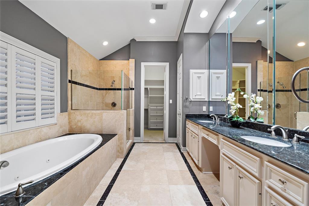 A luxurious spa-like experience awaits in the primary ensuite bath, featuring a glass-enclosed shower, jetted tub, and a vanity area with spacious counters. The tile flooring adds a timeless touch to the space and leads you directly to the sizeable walk-in closet.