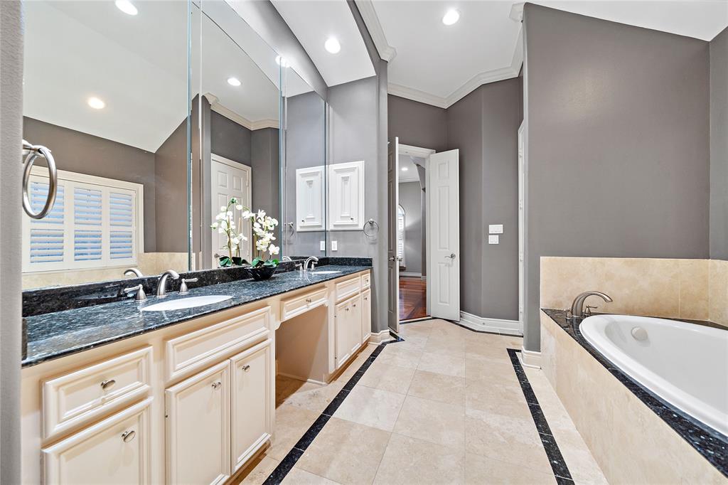 This ensuite bathroom features a vanity area with double sinks, a granite top, sizable mirrors, and built-in cabinetry, allowing for clutter-free storage.