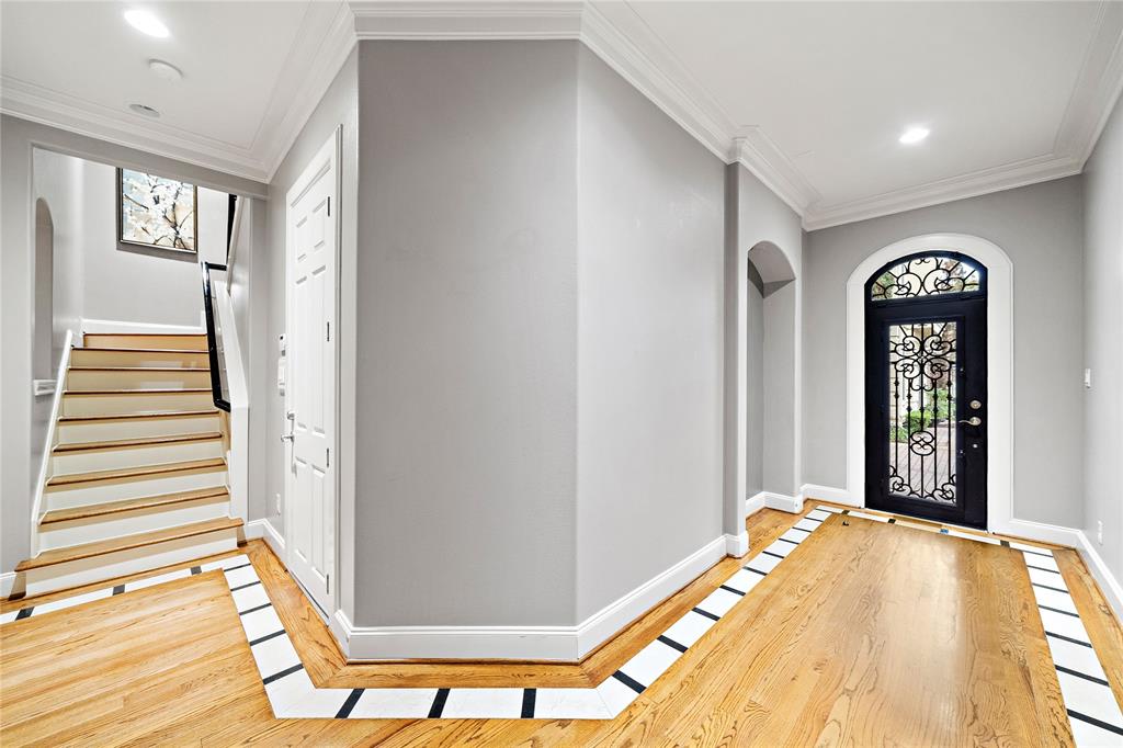 Welcome guests through the elegant foyer, showcasing a custom iron door, recessed wall, and engineered wood floors that add warmth to the space. Enjoy easy access to the garage, a secondary bedroom, and the second-floor areas.
