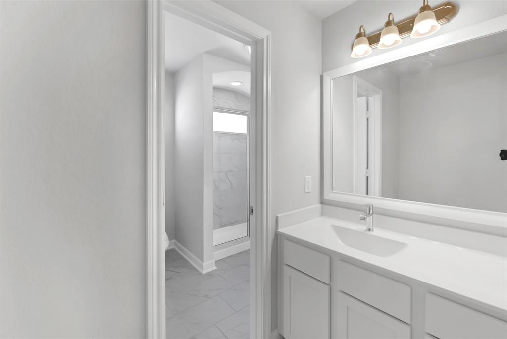 The Jack and Jill bath features tile flooring, bath/shower combo with tile surround, white stained wood cabinets, beautiful light countertops, mirror, dark, sleek fixtures and modern finishes.