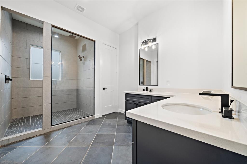 Boasting high ceilings and smooth quartz vanity counters, the ensuite bath comes complete with a glass-enclosed shower featuring custom tiles and a double rain head.