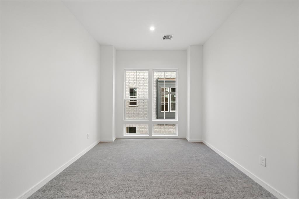 This secondary bedroom comes complete with recessed lighting, a wall of double-pane windows, sleek baseboards, and textured carpet flooring.
