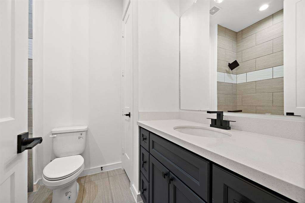 The secondary bathroom showcases a shower/tub combo with a custom tile surround, recessed lighting, and a vanity area with spacious countertops and built-ins for extra storage.