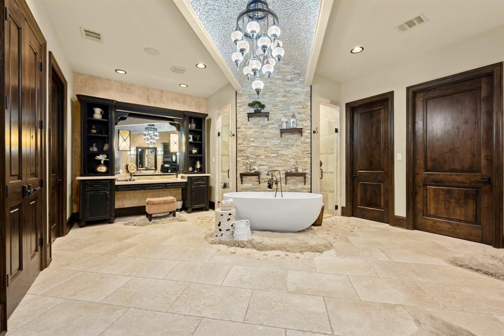 Into the primary bath the barrel ceiling is echoed throughout this space but with a slight Moroccan theme as this custom chandelier lights the area for a soak or shower. Dual vanities and separate water closets for each. Shower has tumbled river rock design and seating with two separate entrances.