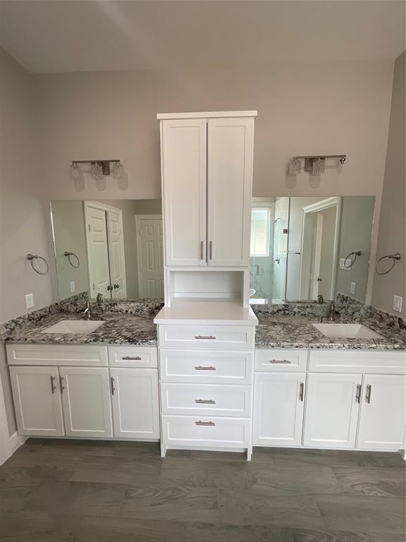 View of primary suite showing dual granite top vanities and custom cabinetry.