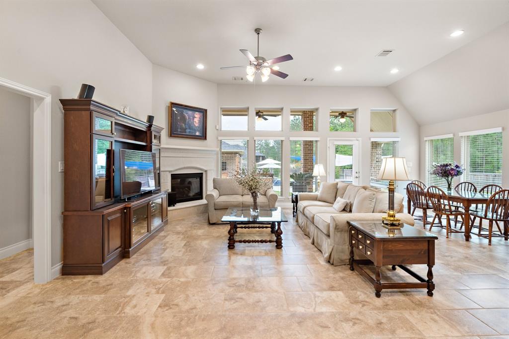 Step into the bright and spacious living area with soaring ceilings, tile flooring, tall windows, and a stone-mantel fireplace. Easily access the backyard through a windowed door, offering seamless indoor and outdoor flow.