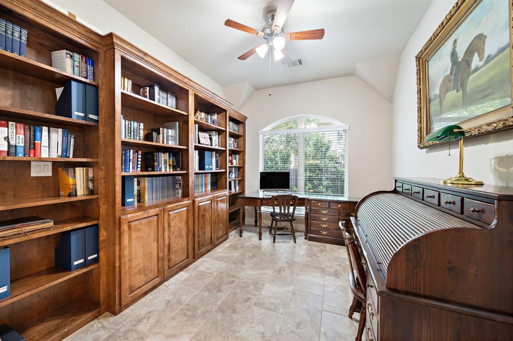 Bright and spacious, the dedicated study/home office is fitted with tile floors, arched windows, built-in bookshelves, and wooden cabinets.