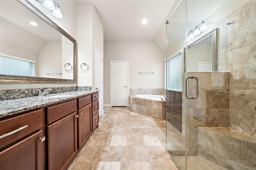 The primary ensuite bathroom showcases tile flooring, dual vanities, a corner garden tub, a glass-enclosed shower, and an oversized walk-in closet.