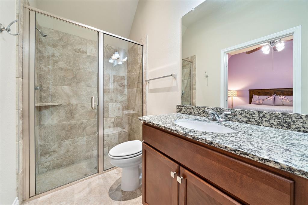 This secondary bathroom features a glass-enclosed shower and a vanity area with a granite countertop, a large mirror, and built-in cabinetry.