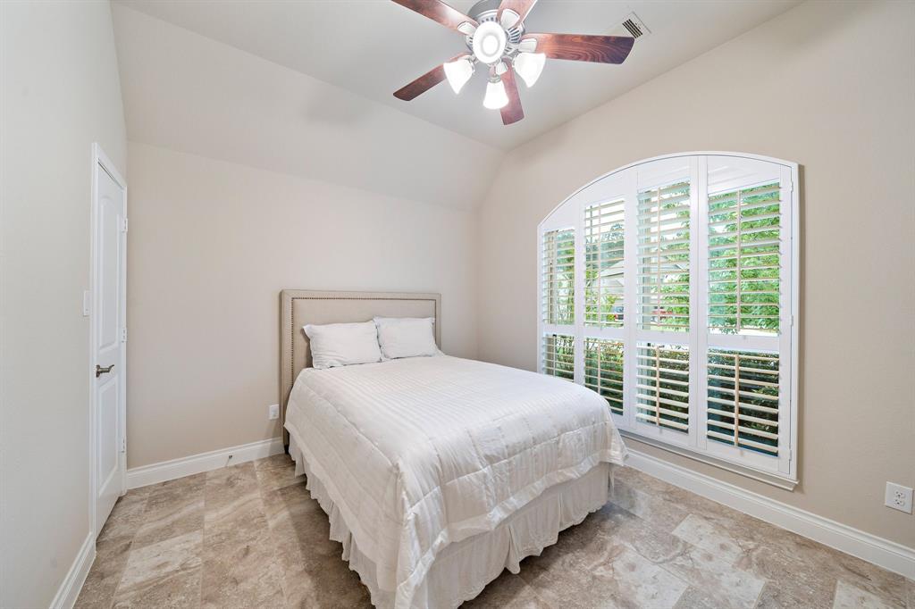 Accessible from the entryway, this secondary bedroom features tile floors, a ceiling fan, a sloped ceiling, and arch windows with shutters and lush neighborhood views.