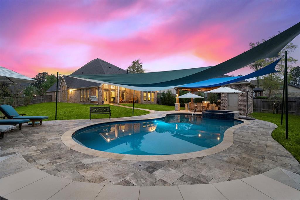Enjoy a refreshing dip in the stunning pool fitted with a spa, parasols, and sunshades—all surrounded by travertine pavers and lush green spaces.