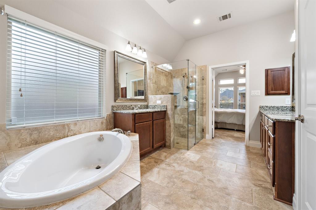A spa-like retreat awaits in the primary ensuite bath, featuring a corner garden tub, a glass-closed shower, a walk-in closet, and dual vanities dressed with granite countertops, built-in cabinets, and large mirrors.