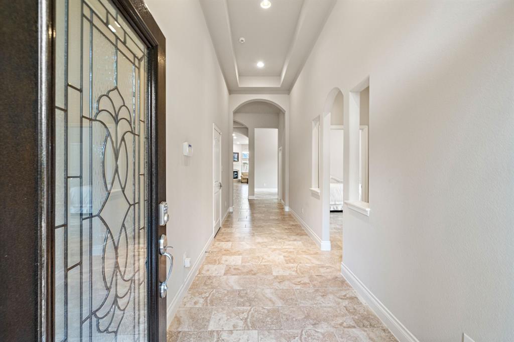 Greet guests in the extended foyer showcasing beautiful tile flooring, tray ceilings, and arched entryways leading to the spacious living areas of the home.