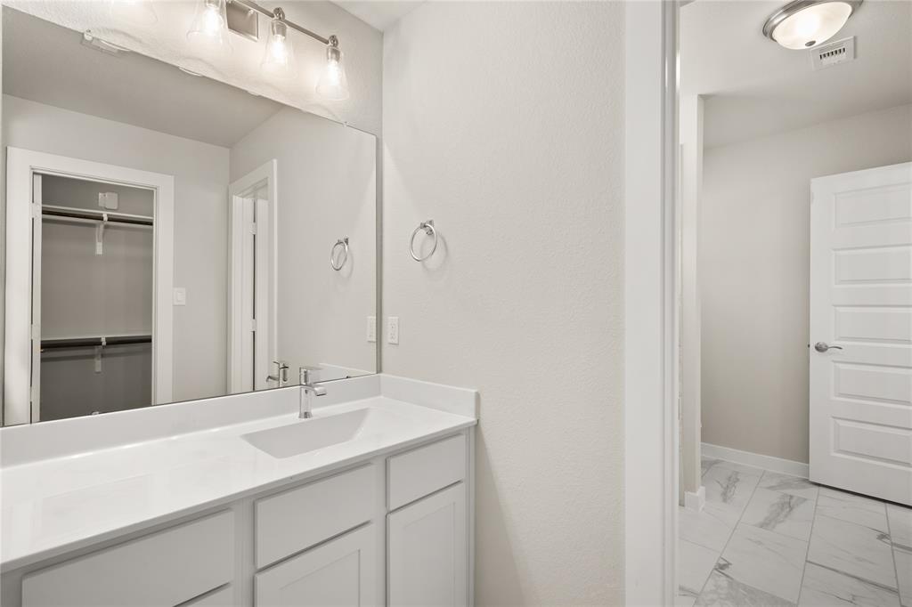 The Jack and Jill bath features tile flooring, bath/shower combo with tile surround, white stained wood cabinets, beautiful light countertops, mirror, dark, sleek fixtures and modern finishes.