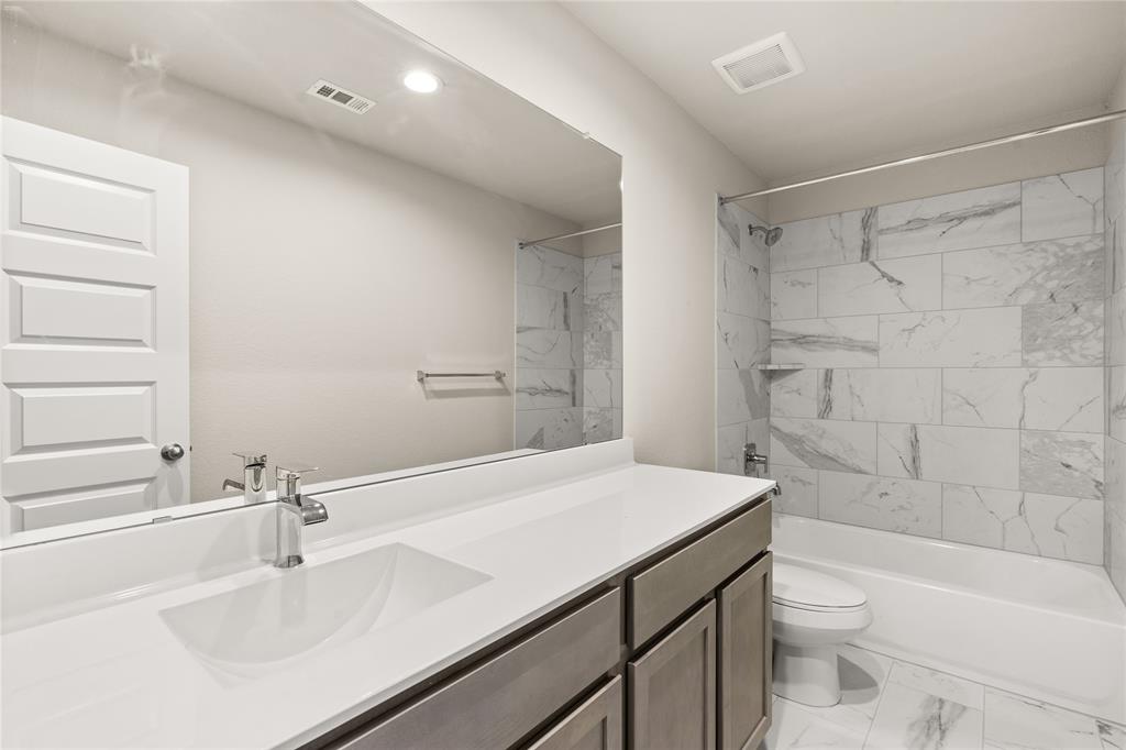 Secondary bath features tile flooring, bath/shower combo with tile surround, dark wood cabinets, beautiful light countertops, mirror, dark, sleek fixtures and modern finishes.