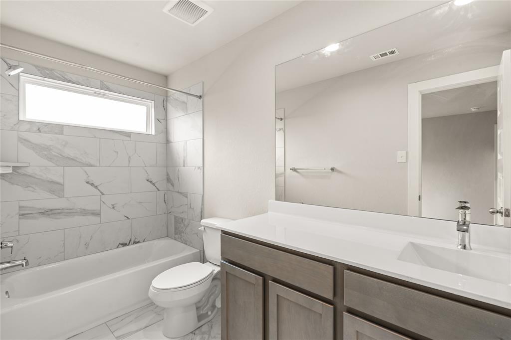 This private bath features tile flooring, bath/shower combo with tile surround, dark wood cabinets, beautiful light countertops, mirror, dark, sleek fixtures and modern finishes.