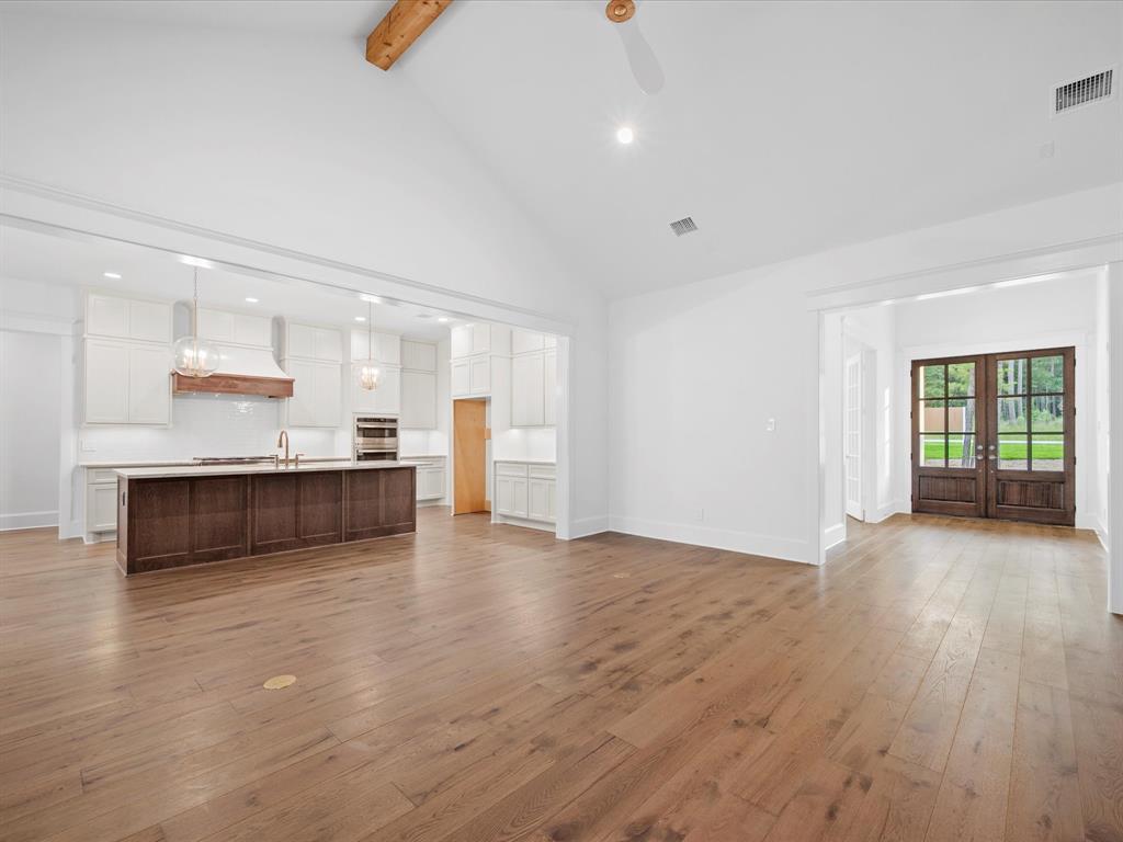 Open plan with vaulted ceiling, accents of hardwood in beams, kitchen island and warm wood floors