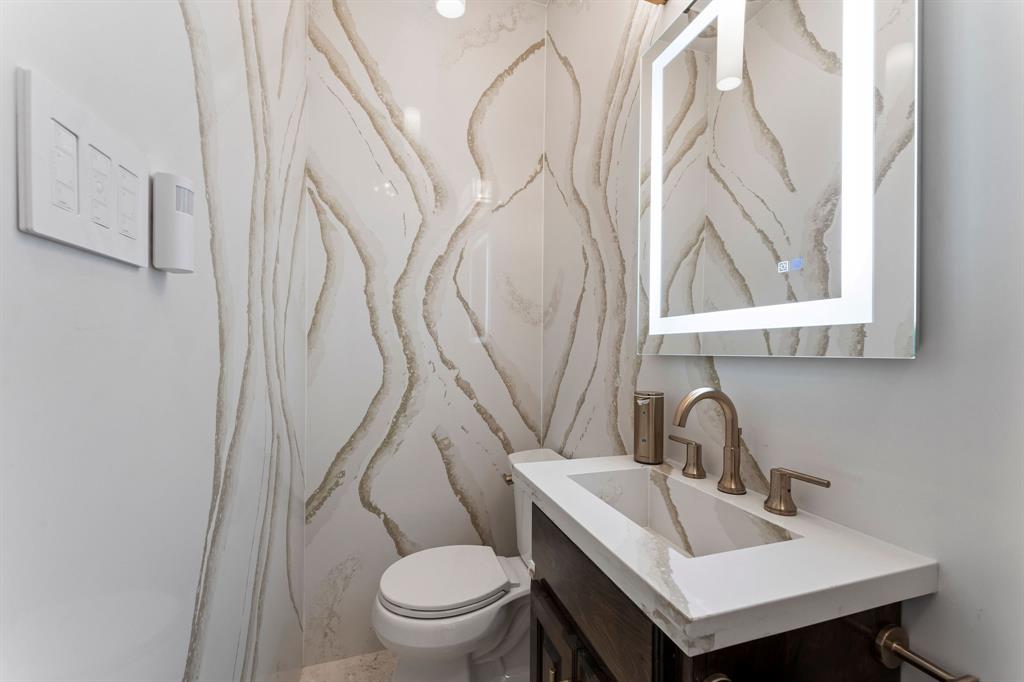 The downstairs half bath features Venezia champagne gold quartz countertop, walls, and ceilings, champagne gold hardware, and a frameless LED mirror.