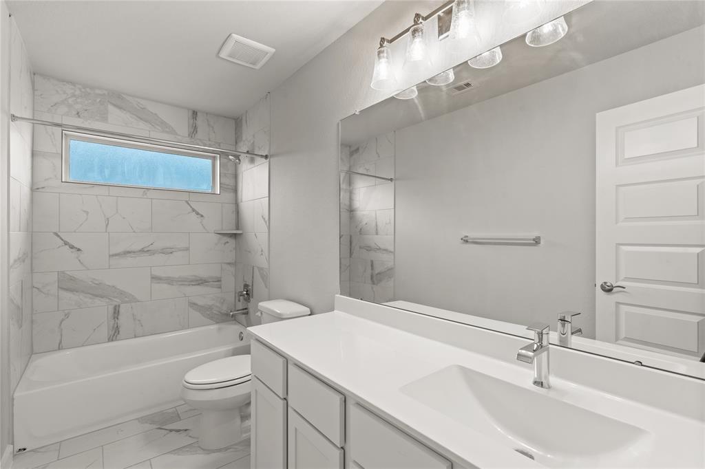 Secondary bath features tile flooring, bath/shower combo with tile surround, cool stained wood cabinets, beautiful light countertops, mirror, dark, sleek fixtures and modern finishes.