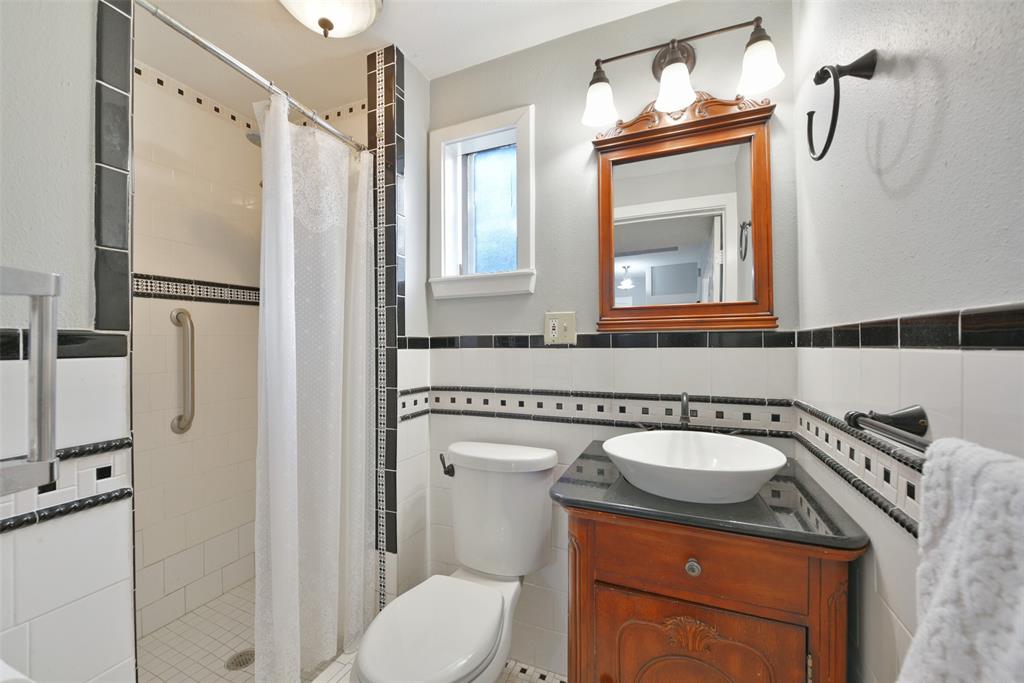 Conveniently located on the first floor, this full bathroom features a timeless black and white tile surround on the walls, floor, and in the walk-in shower, as well as a dresser-style wood vanity with a black granite top and a vessel sink.