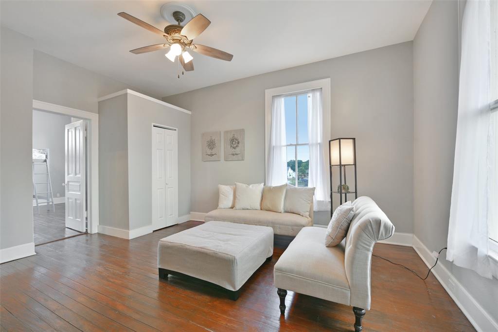 From the second-floor landing, enter this flexible-use space to find elevated ceilings with a lighted ceiling fan, neutral paint, handsome wood floors, a bi-fold door closet, and a pair of sunlit windows with gauzy draperies.