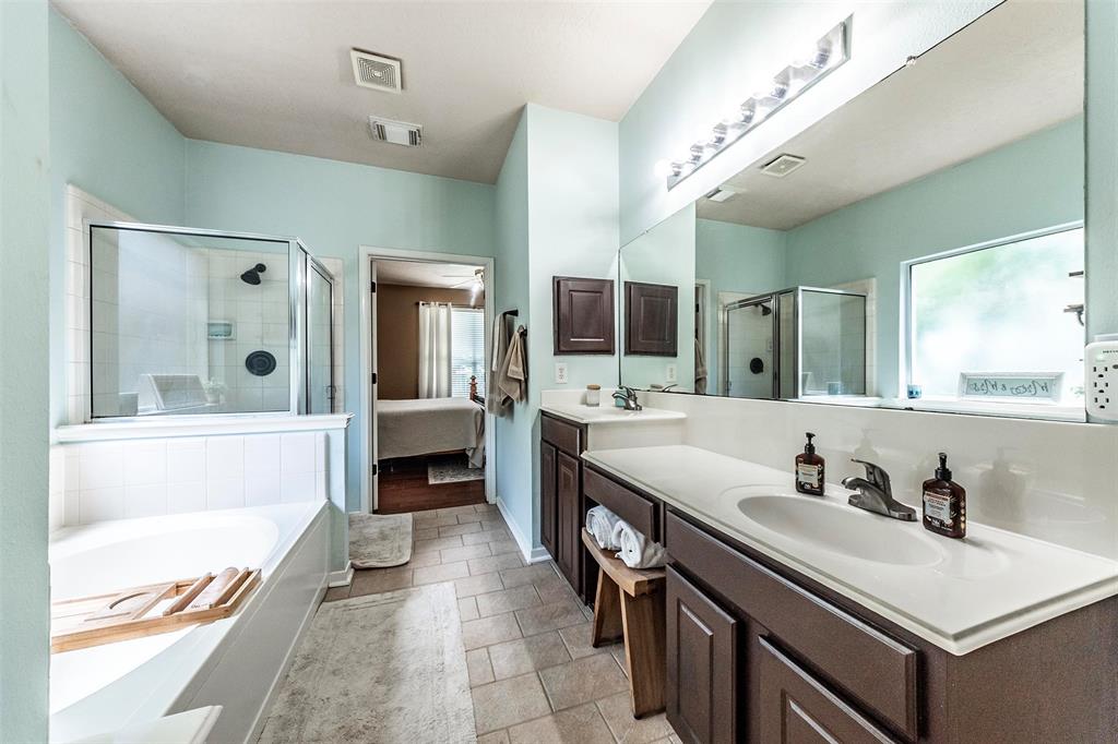 Spa-like primary bathroom with his/her sinks, vanity area, tile flooring, walk-in glass door shower, separate soaking tub and large walk-in closet.
