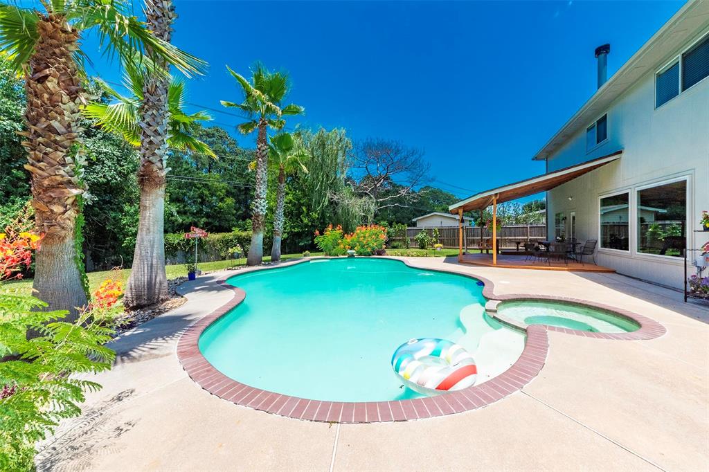 Lush tropical landscaping and mature trees outline the large backyard pool area.