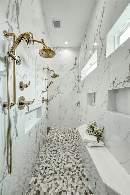 The highlight of the spa-like bath is the double shower. Walls wrapped in porcelain marble tiles include multiple product niches, a bench, and clerestory windows. Brizo rain and hand-held shower heads cloaked in brass are like jewelry in this space.