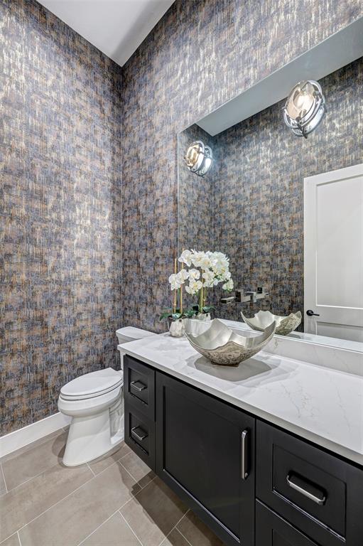 This half bath is located near the foyer. Sitting on top of the floating vanity, the sink is a sculpted work of art! Dramatic wall paper is illuminated by designer wall sconces.