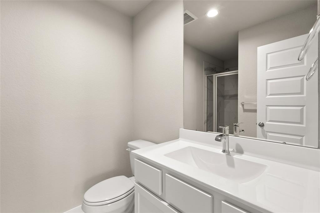 This private bath features tile flooring, shower with tile surround, white stained wood cabinets, beautiful light countertops, mirror, dark, sleek fixtures and modern finishes.